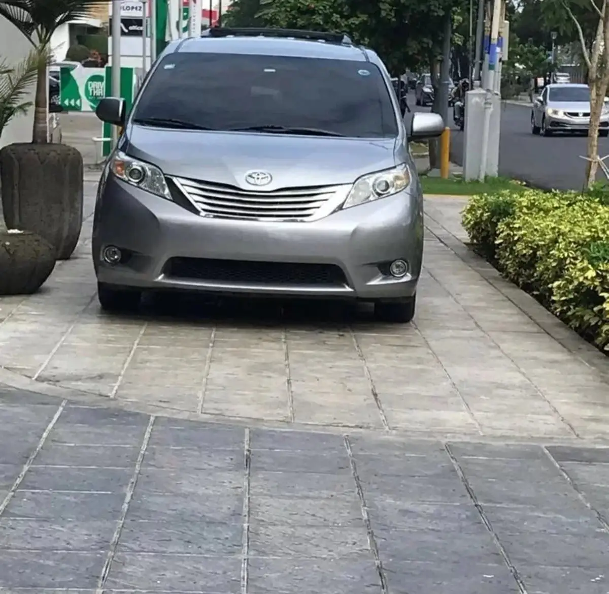 Toyota Sienna plateada estacionada de frente sobre una acera de Santo Domingo, con una bomba de gasolina al fondo