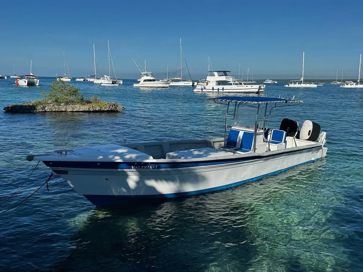 Lancha blanca fondeada en el agua transparente de Bayahíbe, con veleros al fondo