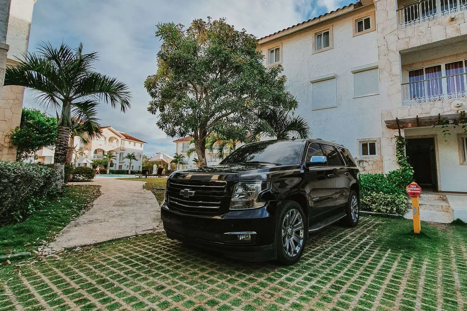 SUV negra estacionada frente a una villa de resort entre palmeras