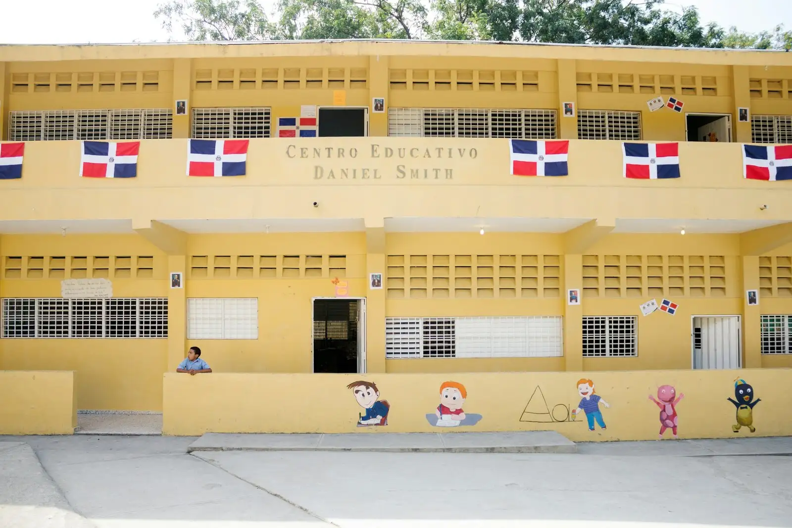 Fachada amarilla de una escuela dominicana con banderas y murales