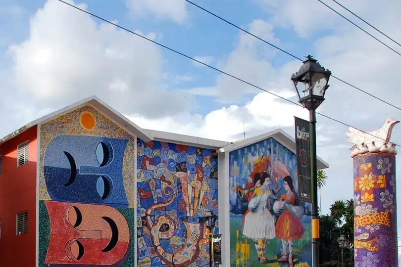 Murales de mosaico de colores en las fachadas de la Plaza de la Cultura de Bonao, junto a un farol y una columna de mosaico con una paloma arriba